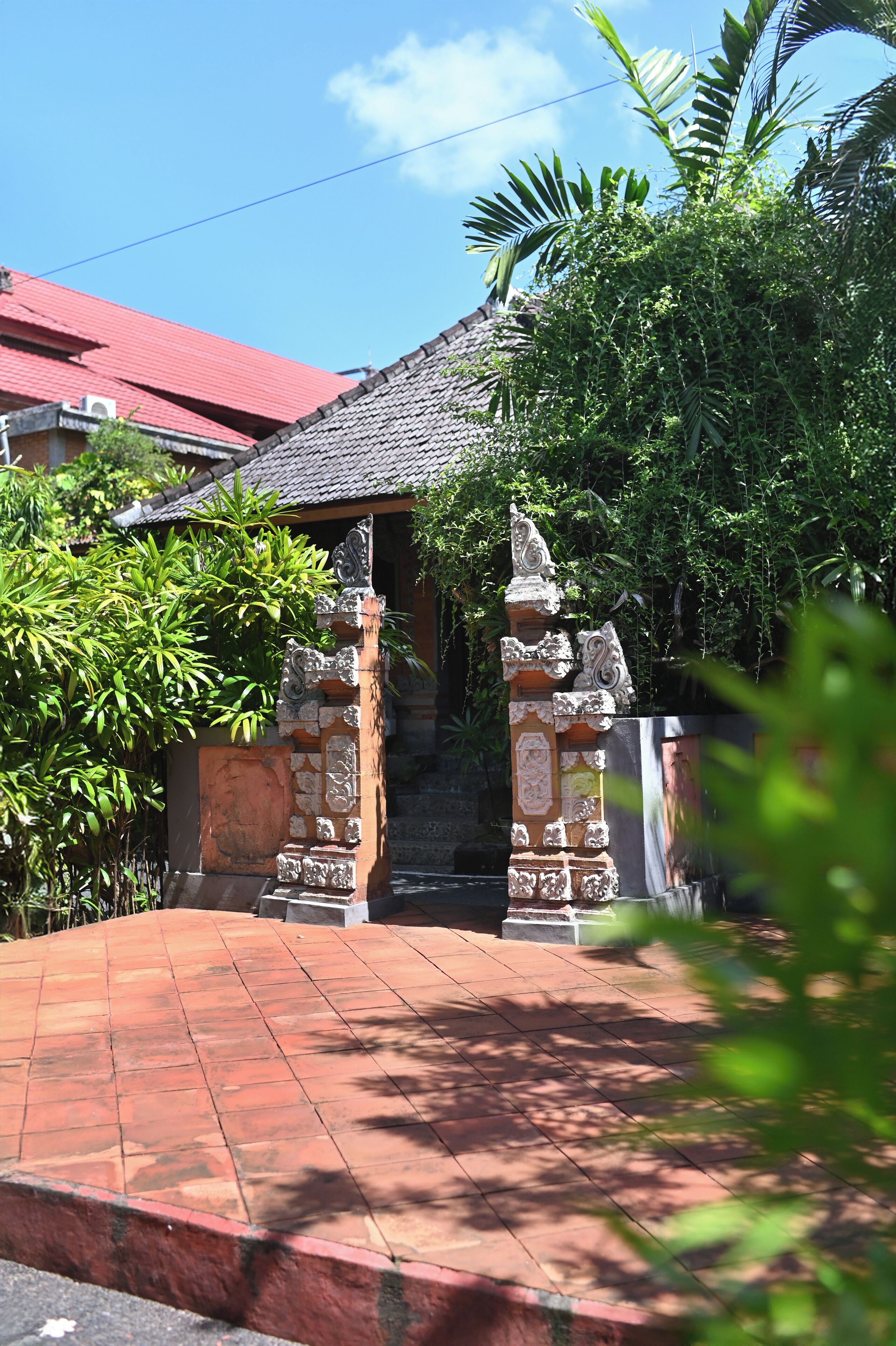 A traditional gate with intricate carvings, leading to a building with a tiled roof and surrounded by lush greenery.