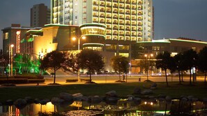 A high-rise hotel with multiple floors, a well-lit facade, and a reflection in a body of water. - Songjiang New Century Grand Hotel Shanghai (Shanghai)