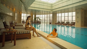 A pool area with lounge chairs and a glass ceiling. - Songjiang New Century Grand Hotel Shanghai (Shanghai)