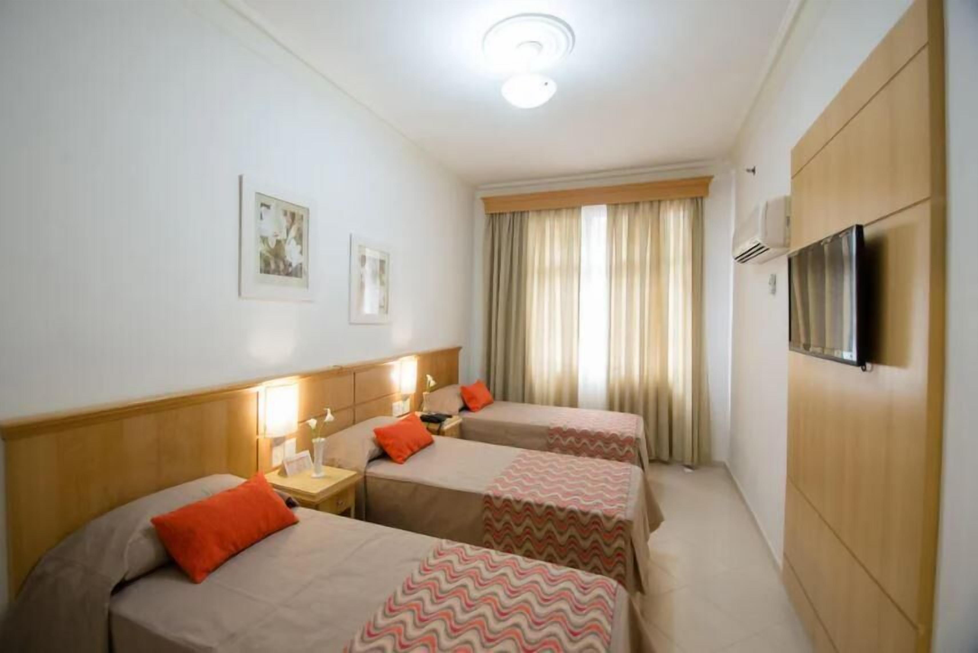 Habitación de hotel con dos camas, televisión y ventana con cortinas.