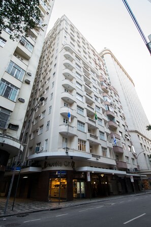 Hotel de vários andares com varandas, restaurante no térreo e uma bandeira visível.