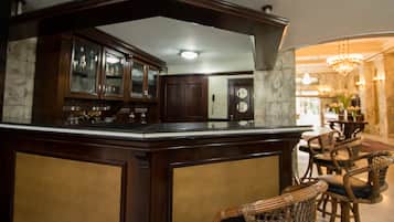 A bar area with dark wood cabinetry and a marble countertop. There are wicker chairs and a chandelier in the background.