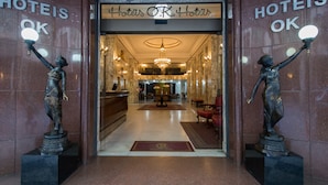 A hotel lobby with marble walls, a chandelier, and two statues holding light fixtures. - Hotel OK (Rio de Janeiro)
