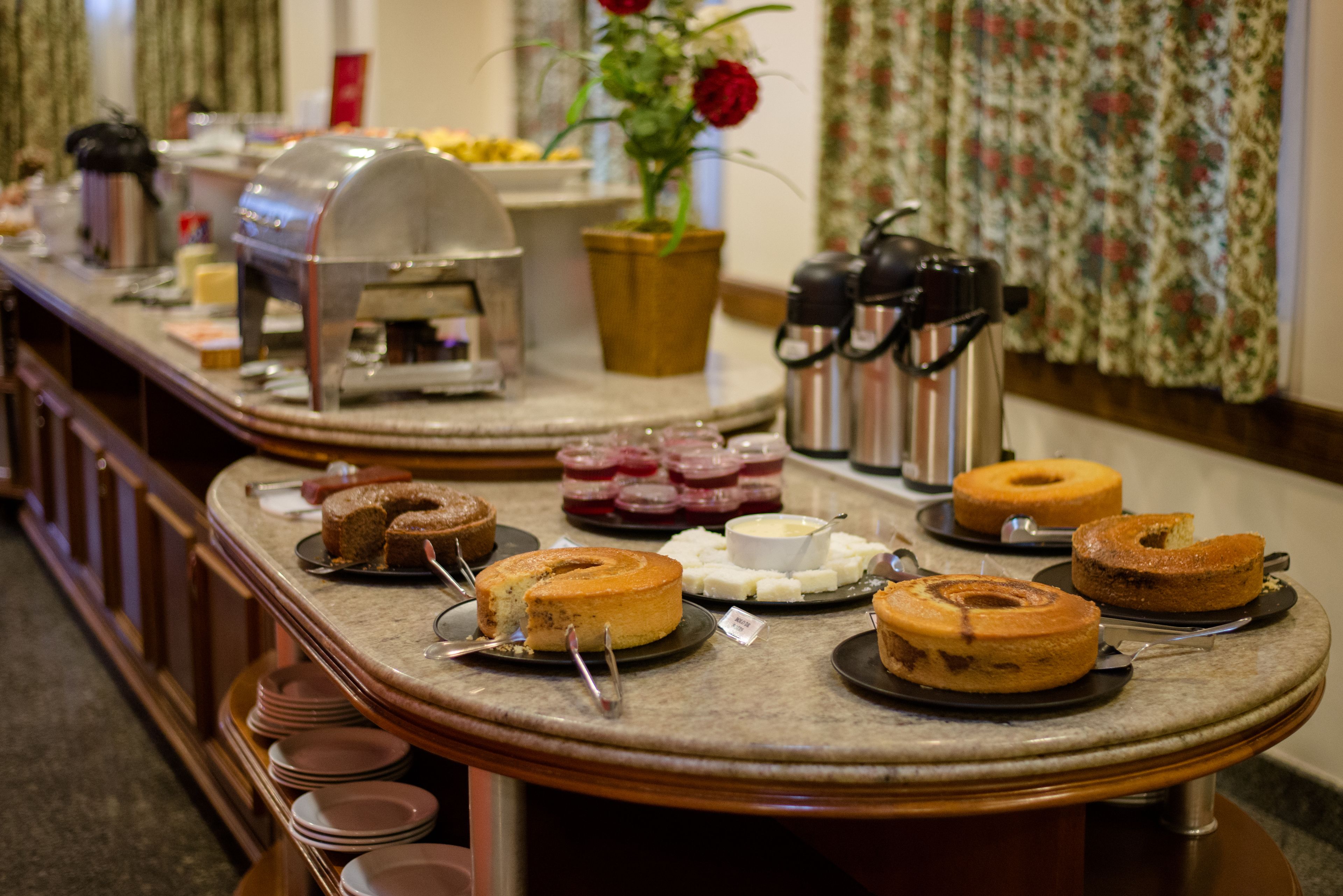 A buffet counter with various cakes and pastries, a coffee machine, and a flower arrangement.