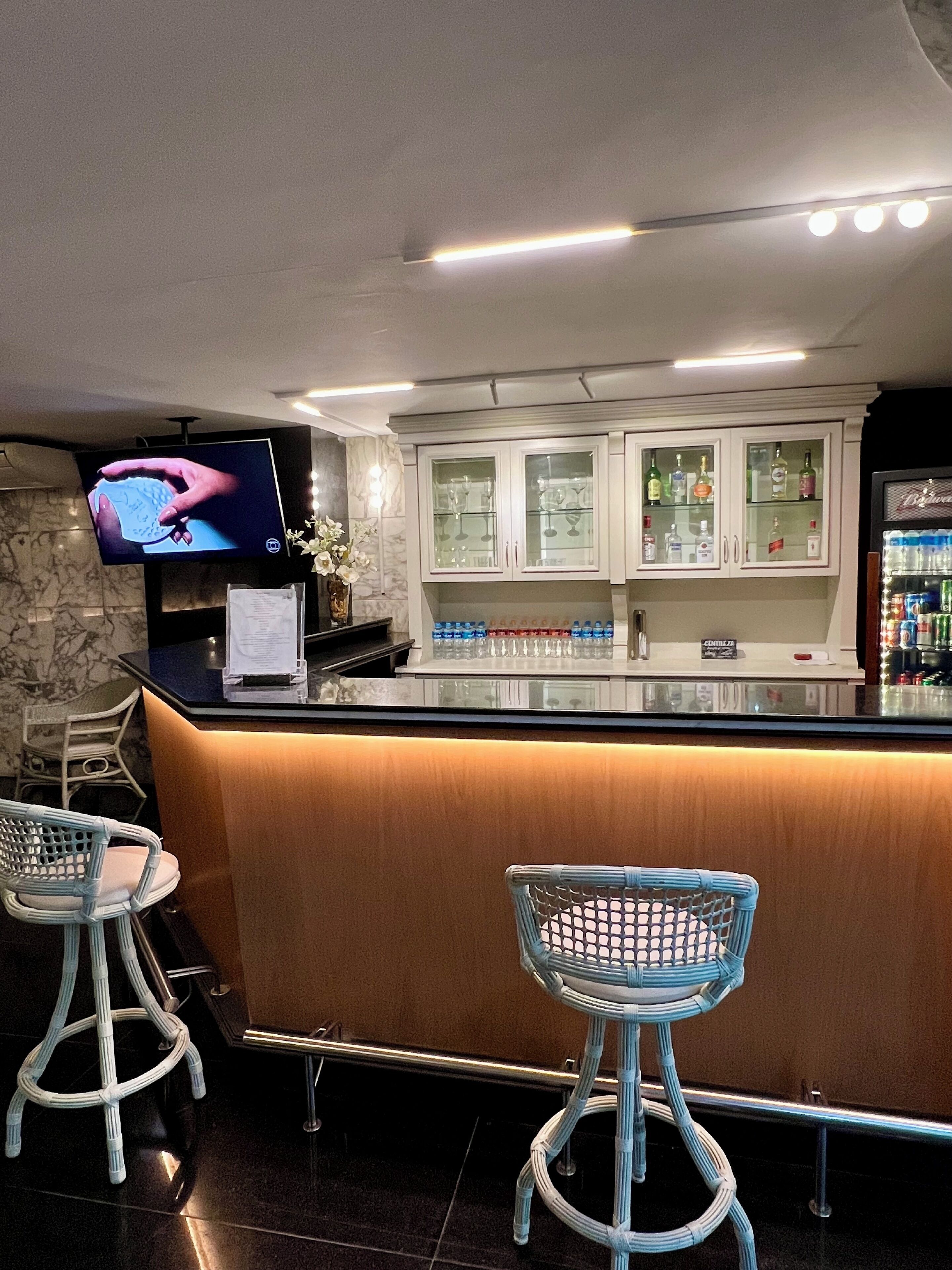A bar area with a counter, bar stools, a television mounted on the wall, and a cabinet with bottles.