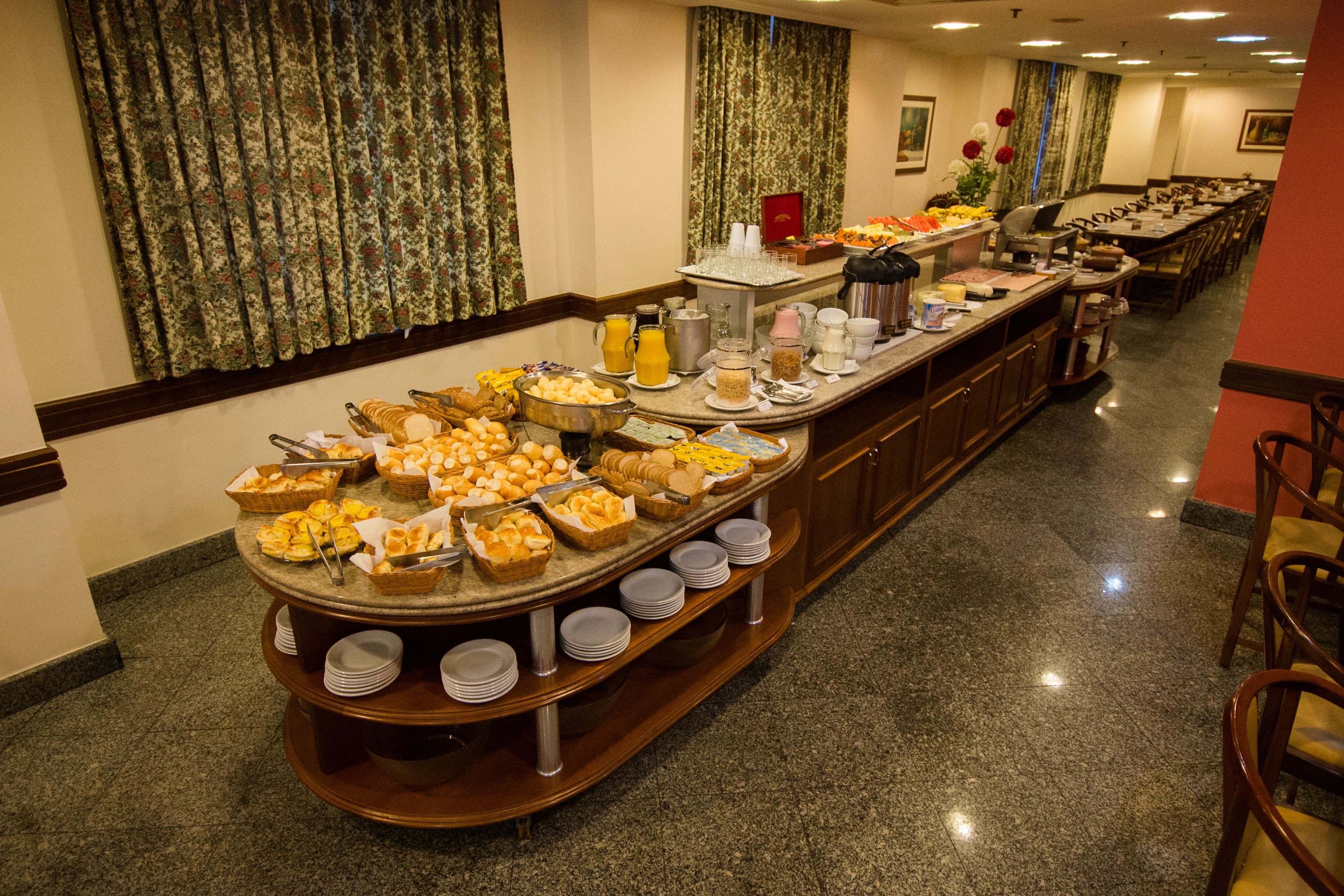 Una barra de buffet con diversos alimentos y bebidas, dispuesta sobre un mostrador largo con piso de baldosas.