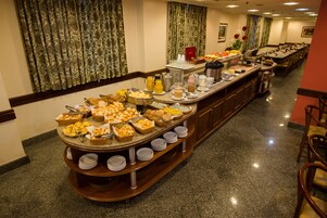 A buffet setup with various food items and beverages, arranged on a long counter with a tiled floor.