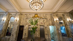 A lobby with marble walls, a chandelier, and two elevators. - Hotel OK (Rio de Janeiro)