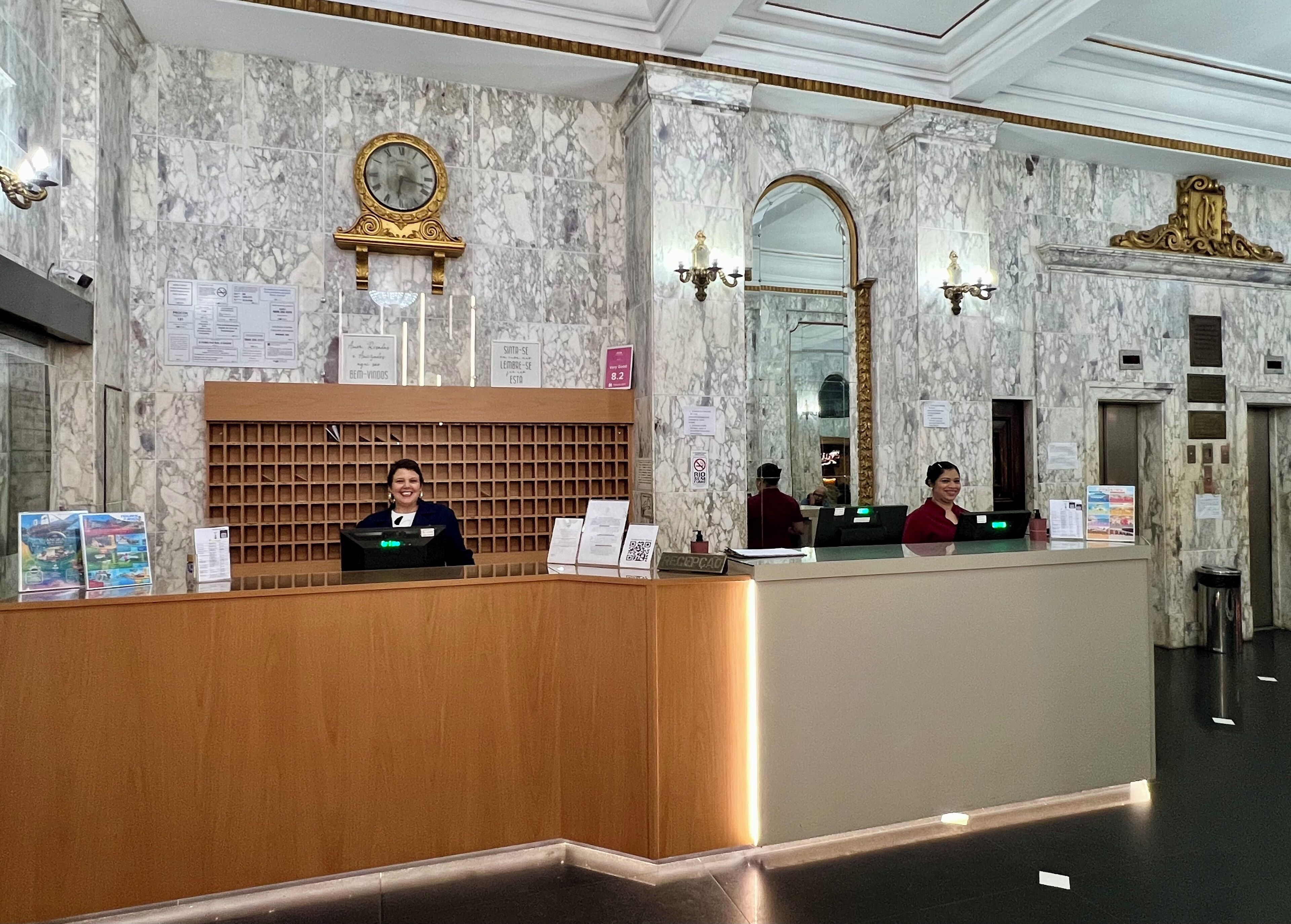 A marble reception desk with a clock, a mirror, and a chandelier.