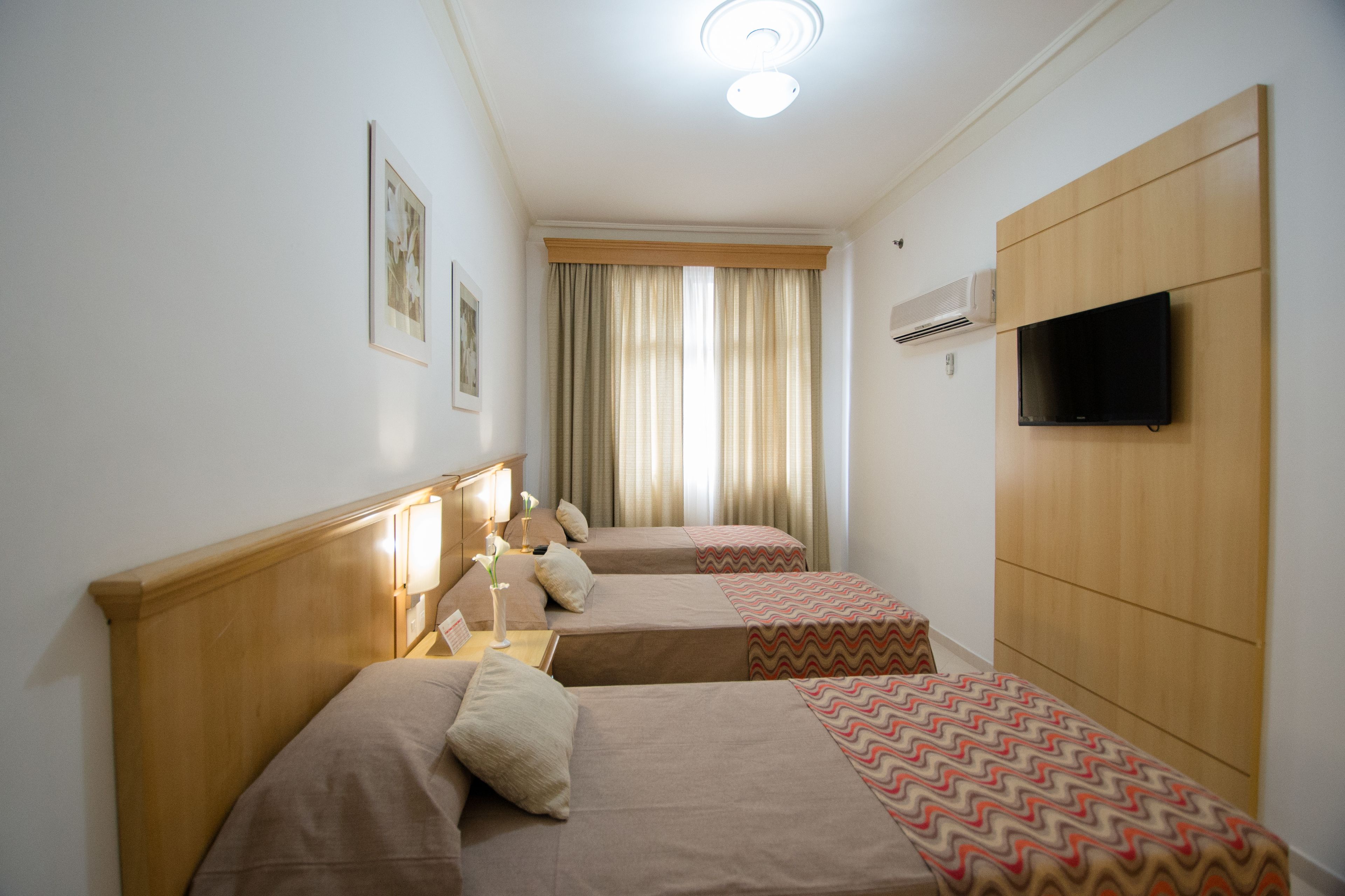 Habitación de hotel con dos camas, televisión y ventana con cortinas.