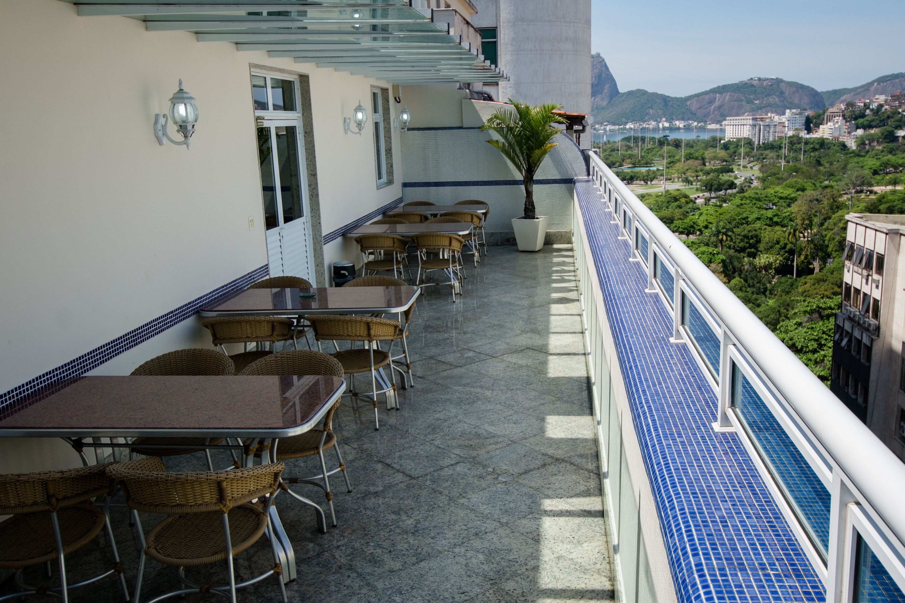 A balcony with tables and chairs, a potted plant, and a view of the city and mountains.