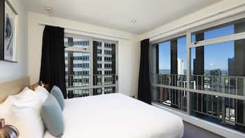 A hotel room with a large bed, a view of the city through floor-to-ceiling windows, and a cityscape visible outside.