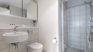 A modern bathroom with a white sink, toilet, and glass-enclosed shower. - Auckland Harbour Suites (Auckland)