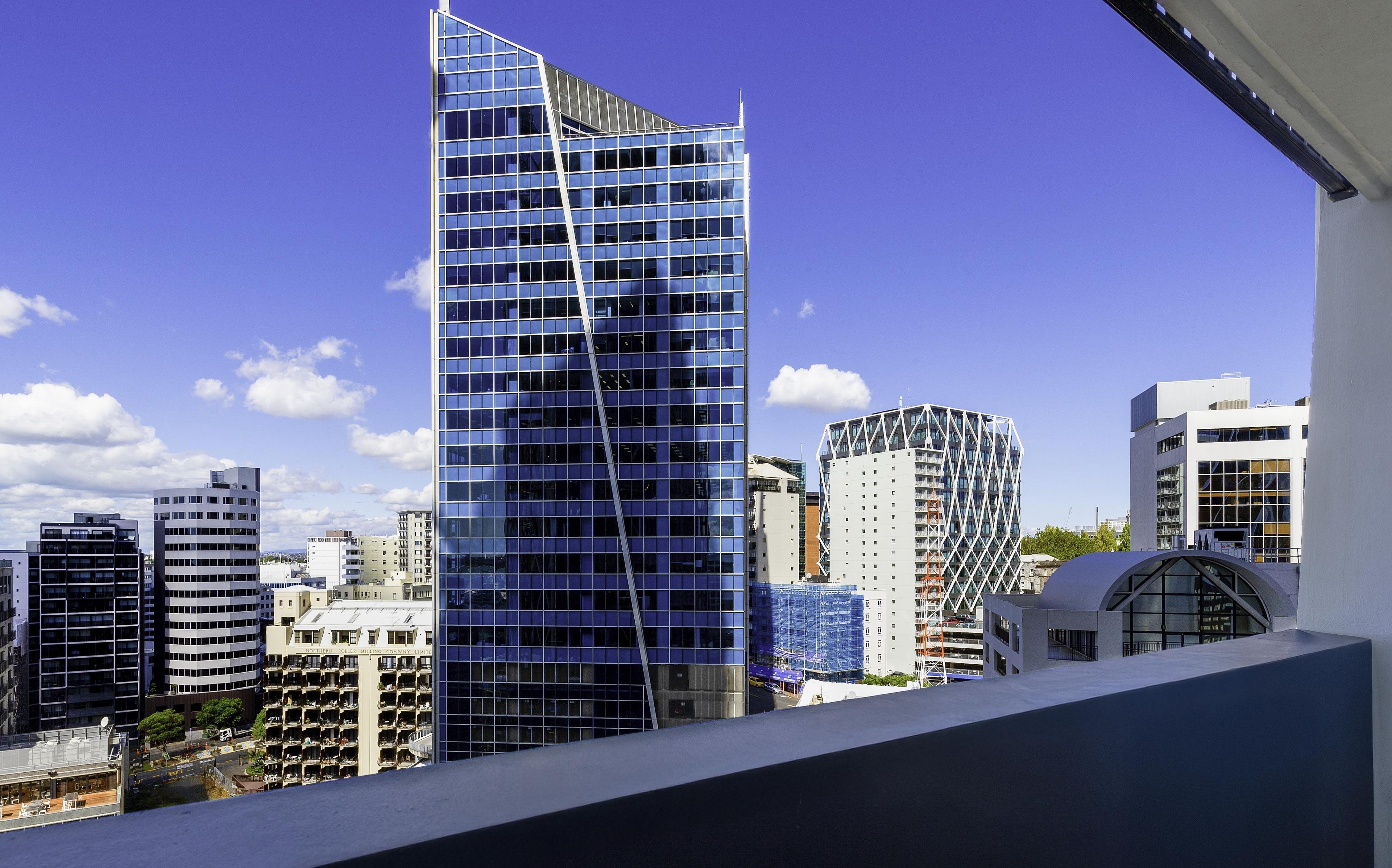 Un edificio moderno de gran altura con un diseño angular distintivo, rodeado de otros edificios contemporáneos.
