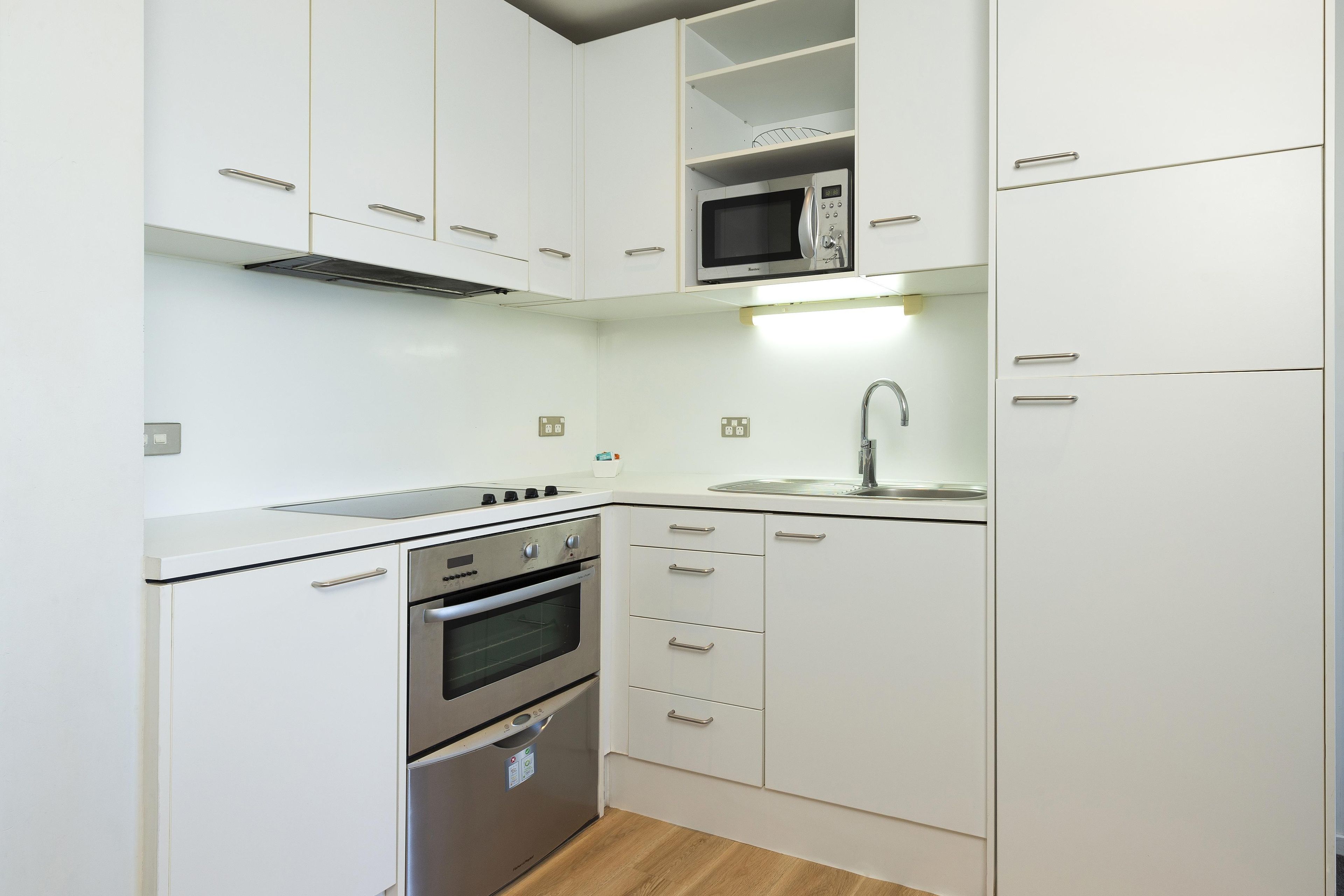 A compact kitchen with white cabinetry, a built-in microwave, a stove, and a sink.