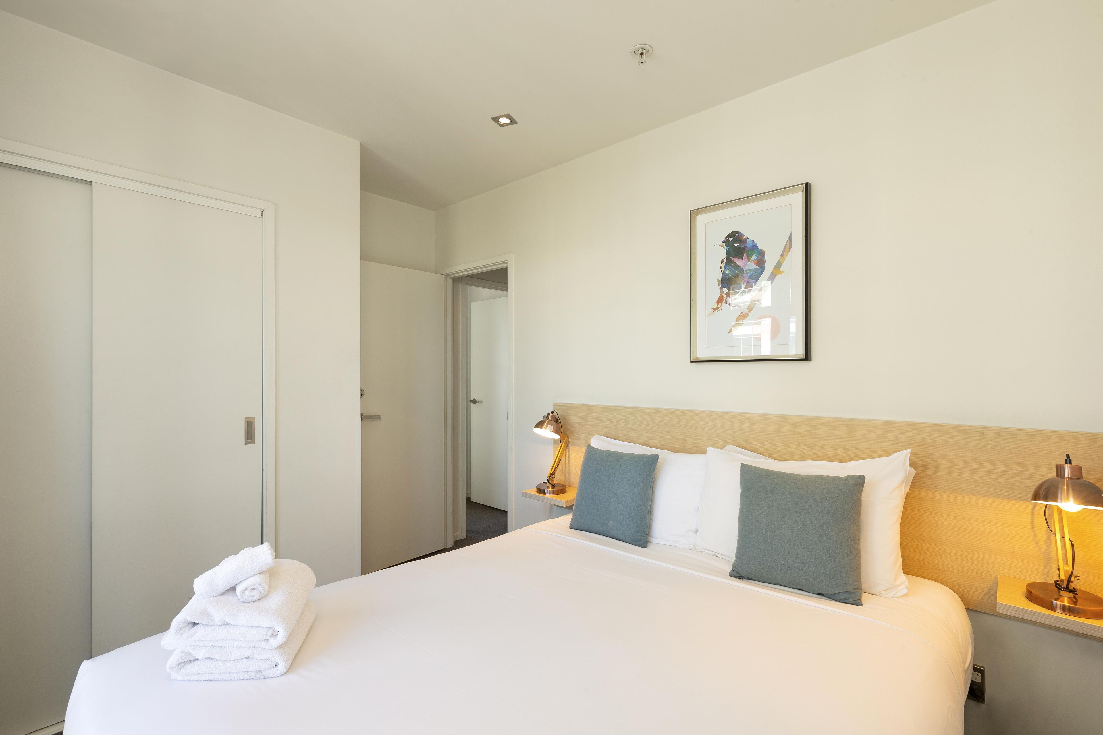 A hotel room with a neatly made bed, a framed artwork on the wall, and a door leading to another room.