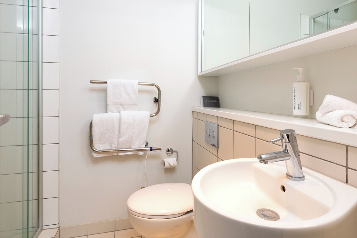 A bathroom with a glass shower enclosure, a toilet, a sink with a mirror above it, and a towel rack with two towels.