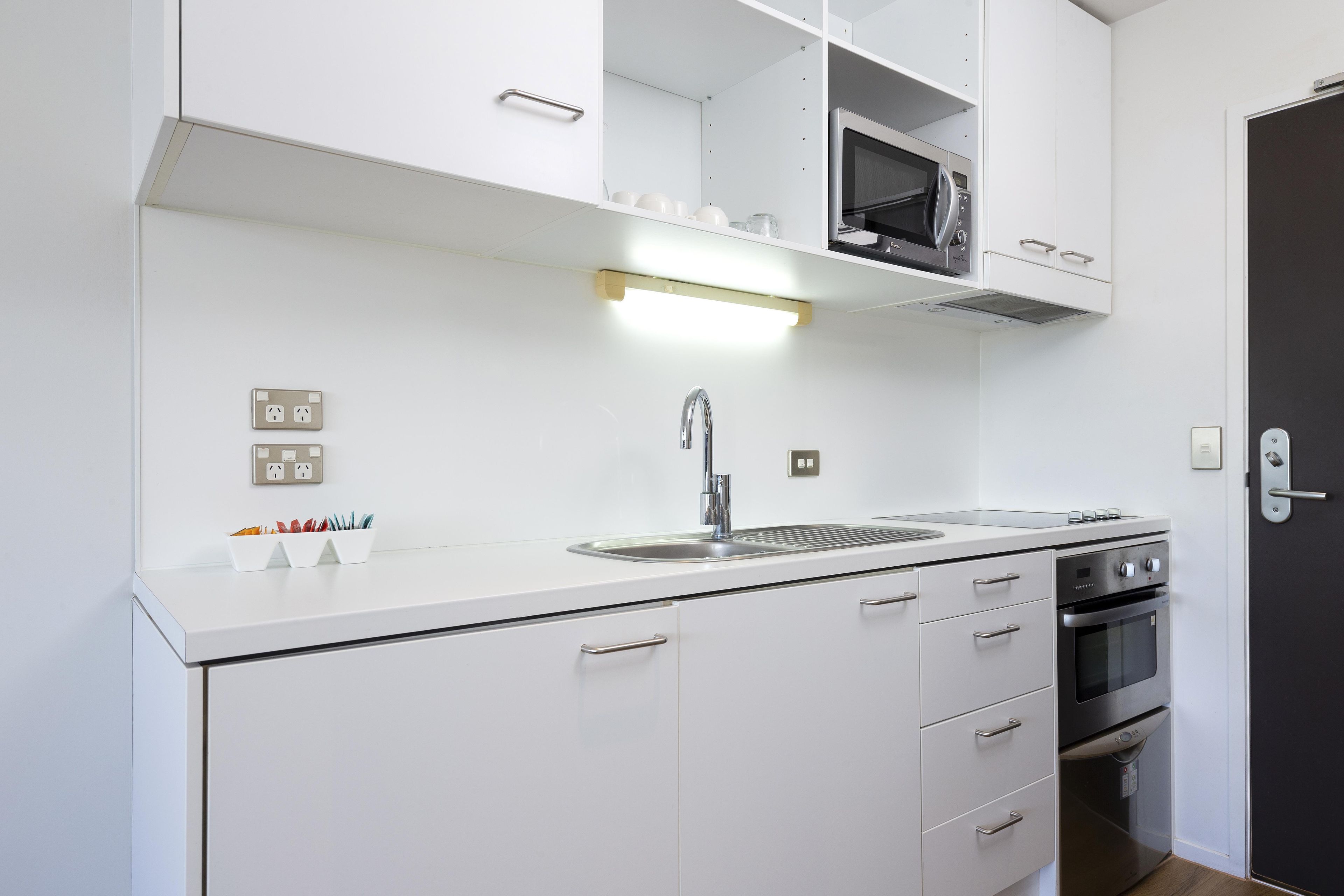 A compact kitchen with white cabinetry, a stainless steel sink, a microwave, and a built-in oven.