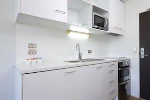 Cozinha compacta com armários brancos, pia de aço inoxidável, micro-ondas e forno embutido.