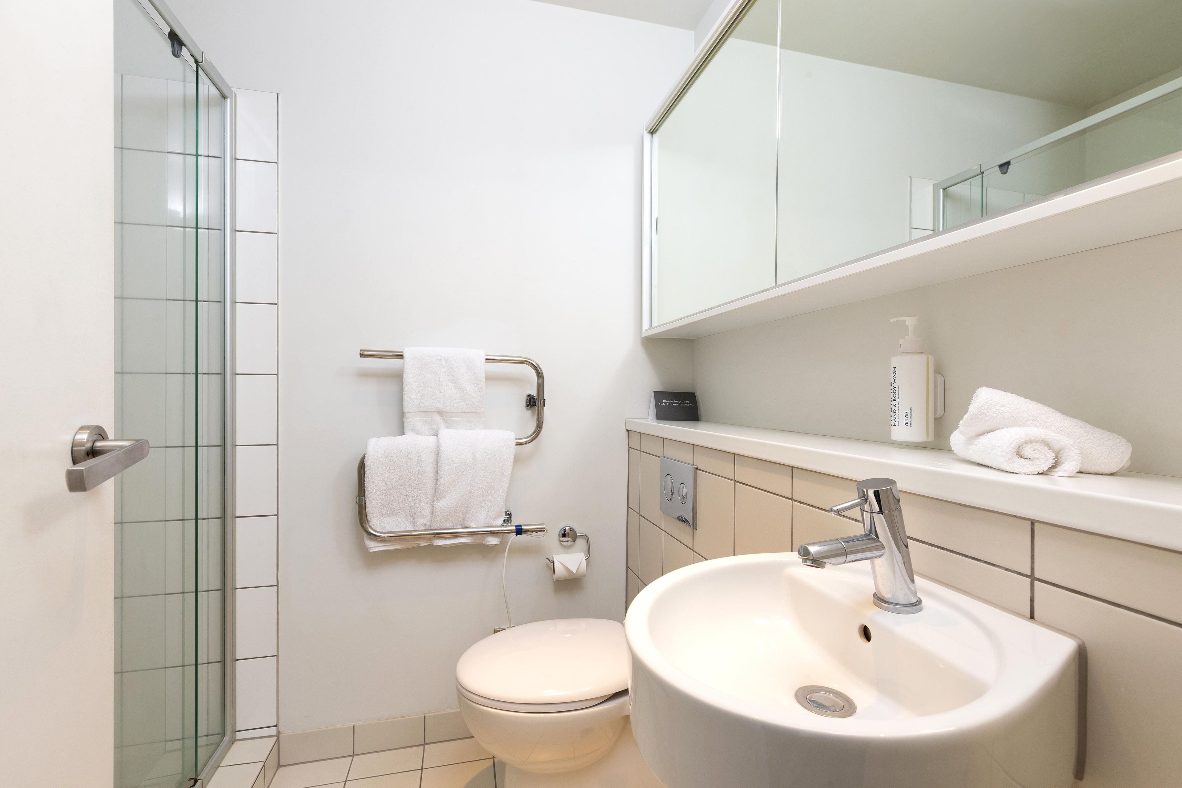 Un bagno moderno con cabina doccia in vetro, un water, un lavandino e uno specchio sopra il piano di lavoro.