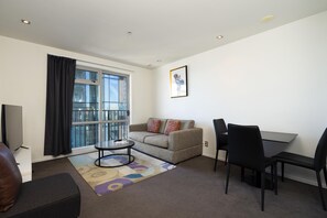 A modern living room with a sofa, a coffee table, a TV, and a dining area with chairs and a table. - Auckland Harbour Suites (Auckland)