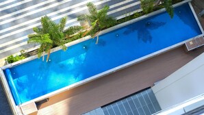 A rectangular swimming pool with a tiled deck surrounding it, bordered by a variety of plants and trees. - Auckland Harbour Suites (Auckland)