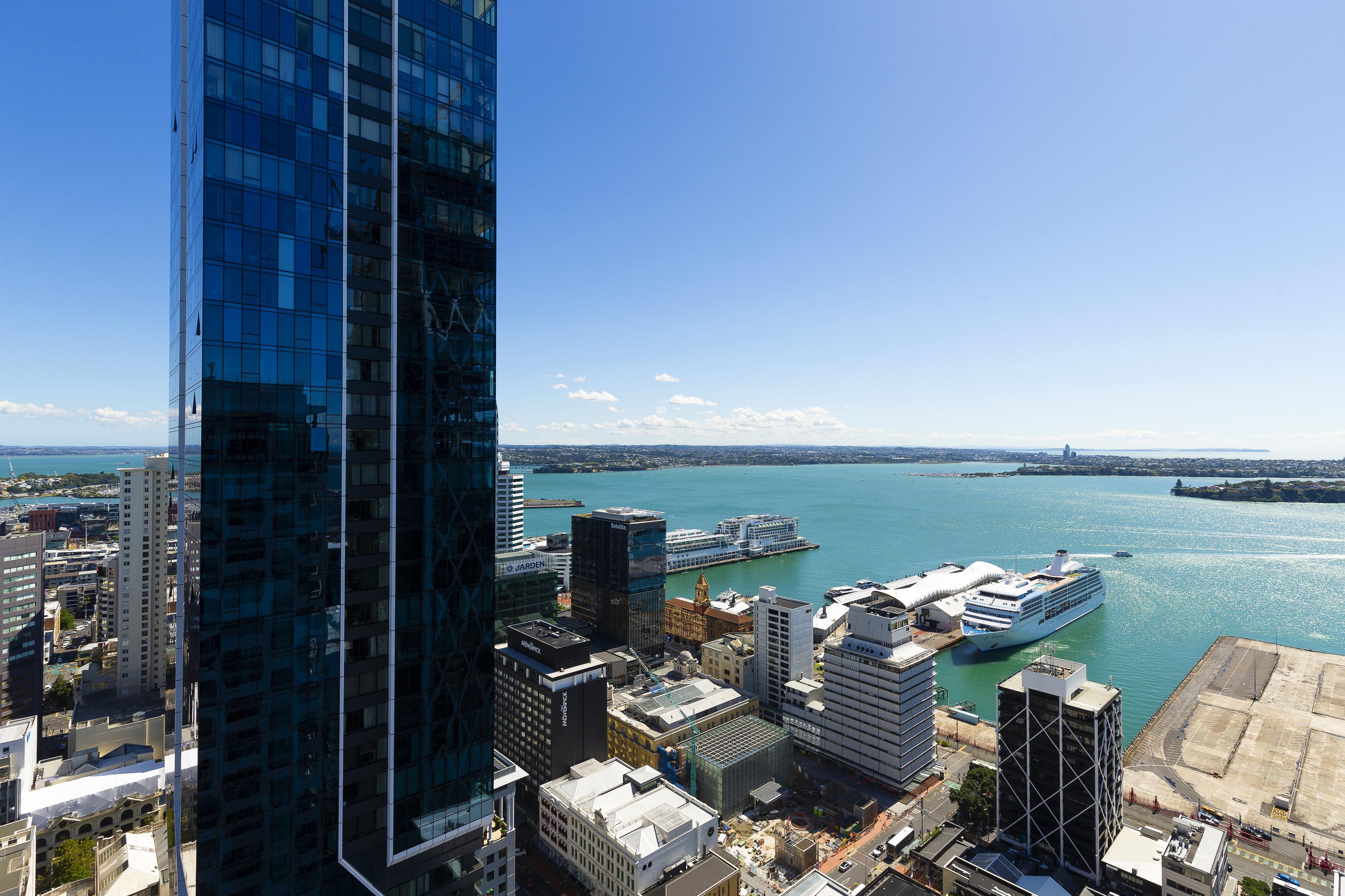 A high-rise building with a glass facade overlooking a waterfront with a cruise ship docked.