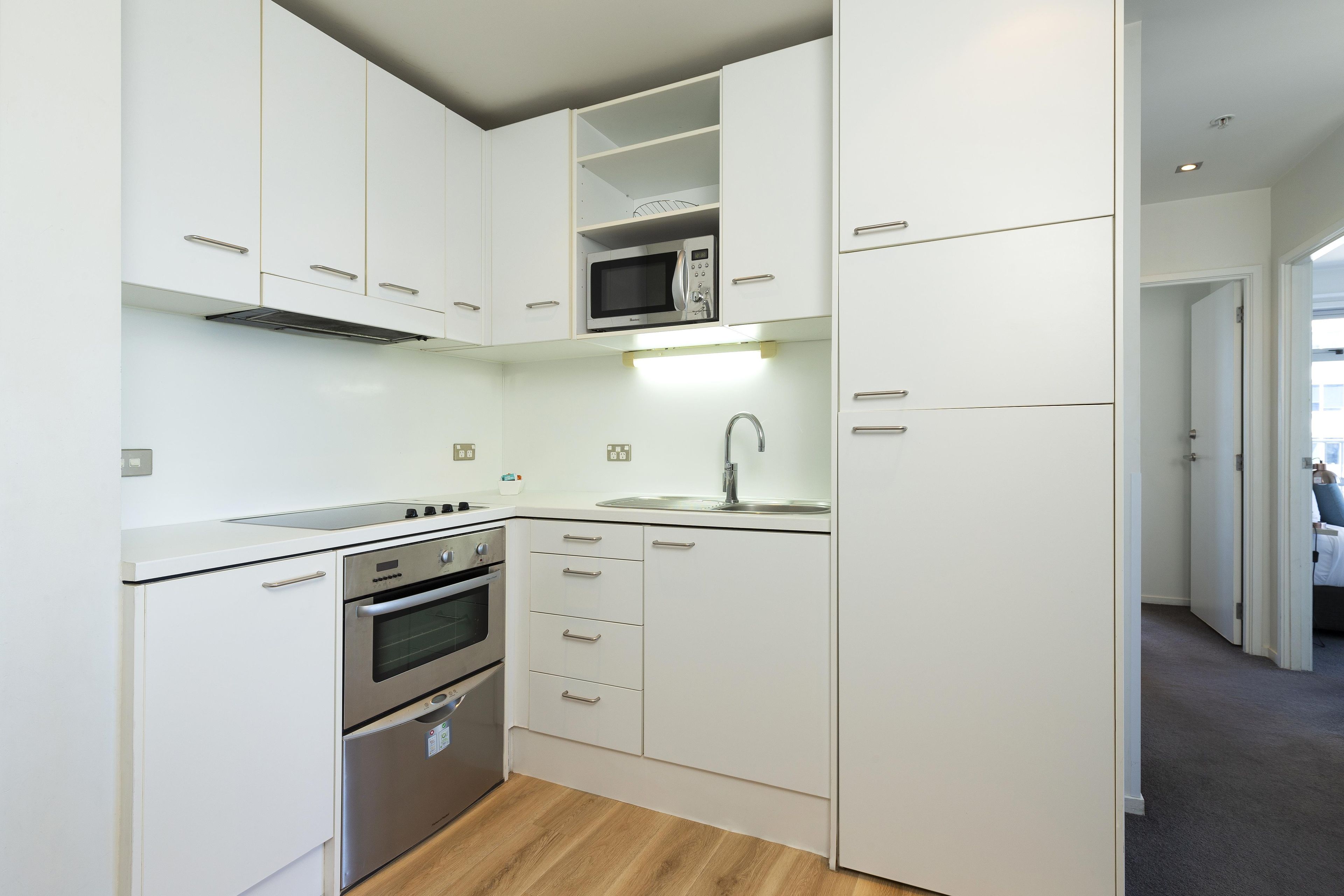 A compact kitchen with white cabinetry, a built-in microwave, a stainless steel oven, and a sink.