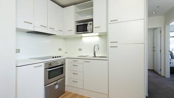 A compact kitchen with white cabinetry, a built-in microwave, a stainless steel oven, and a sink.