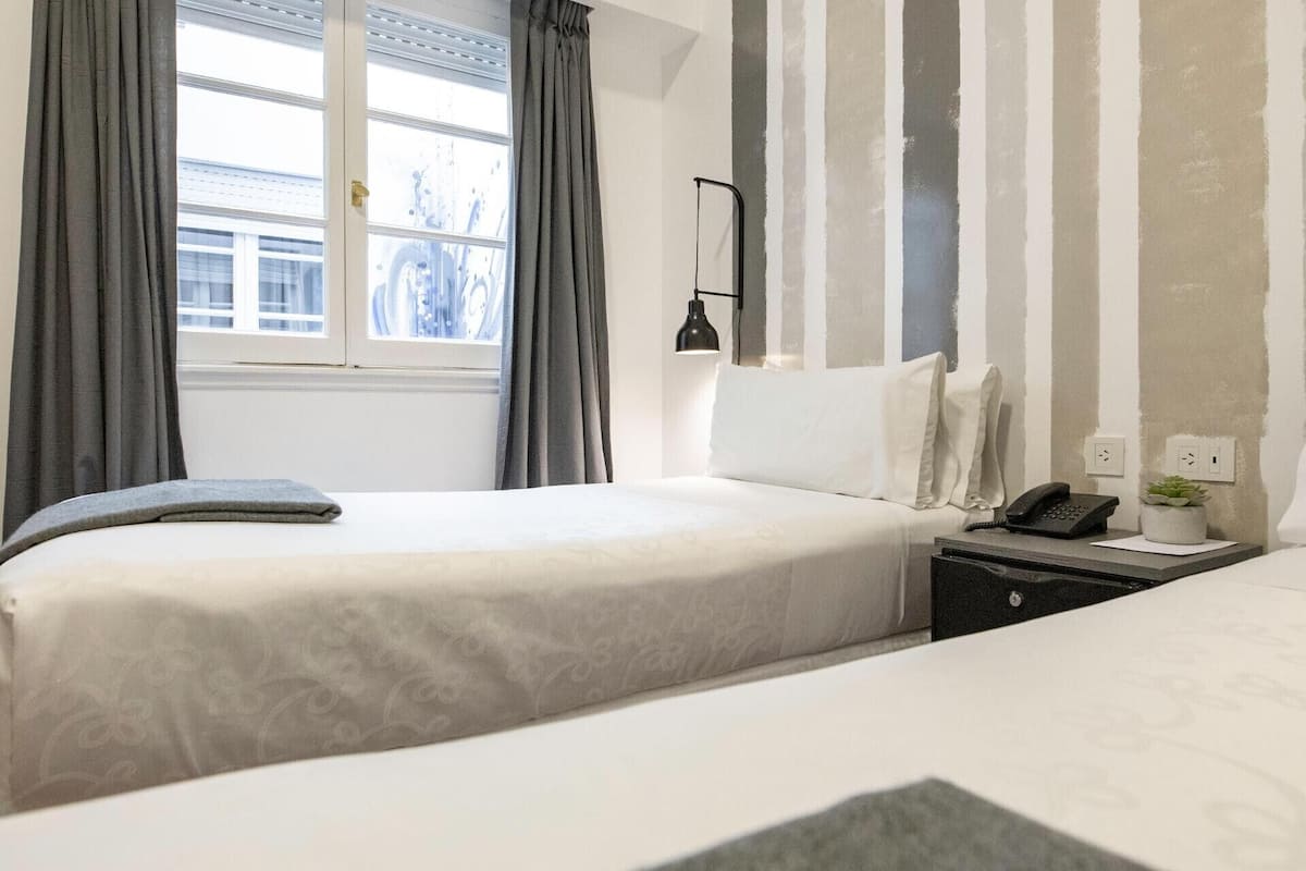 Een hotelkamer met een bed, nachtkastje, lamp en een raam met gordijnen.