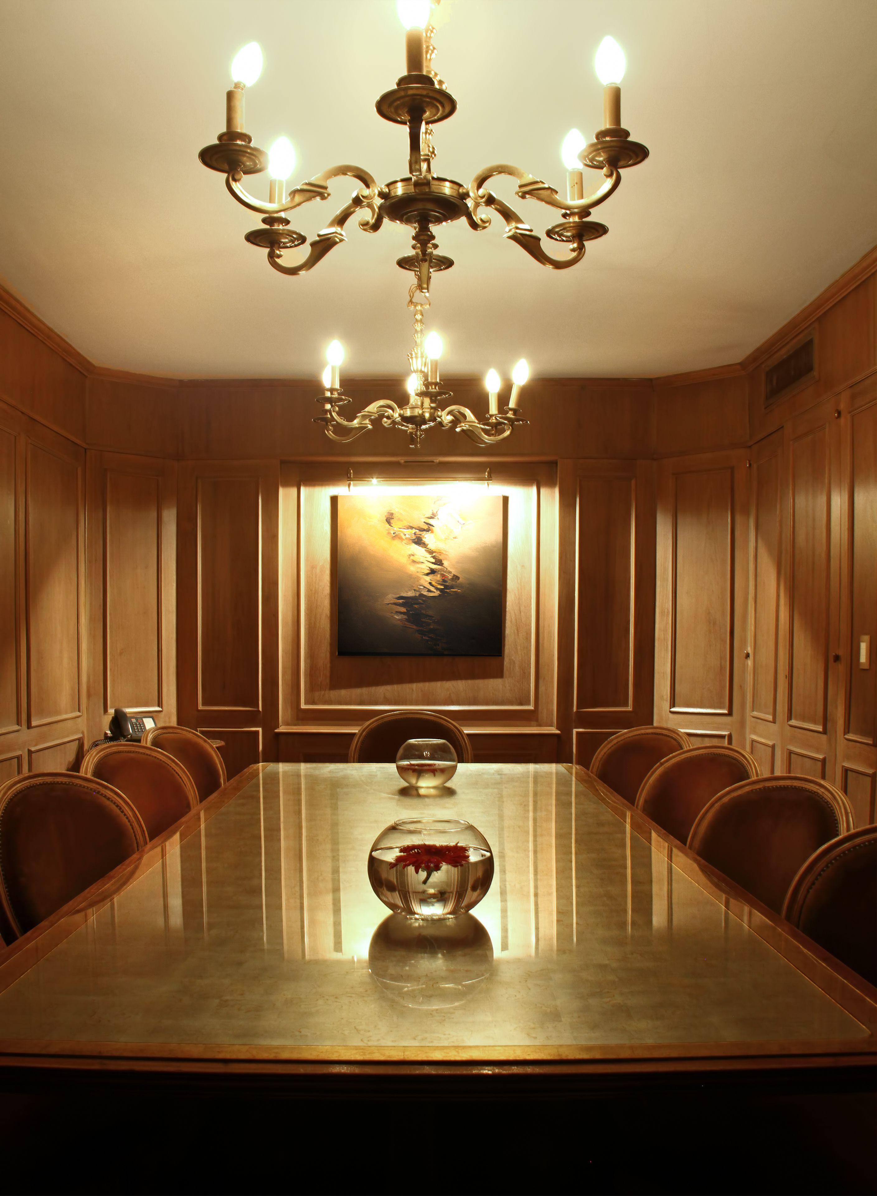 A conference room with a large oval table, wooden paneling, a chandelier, and a painting on the wall.