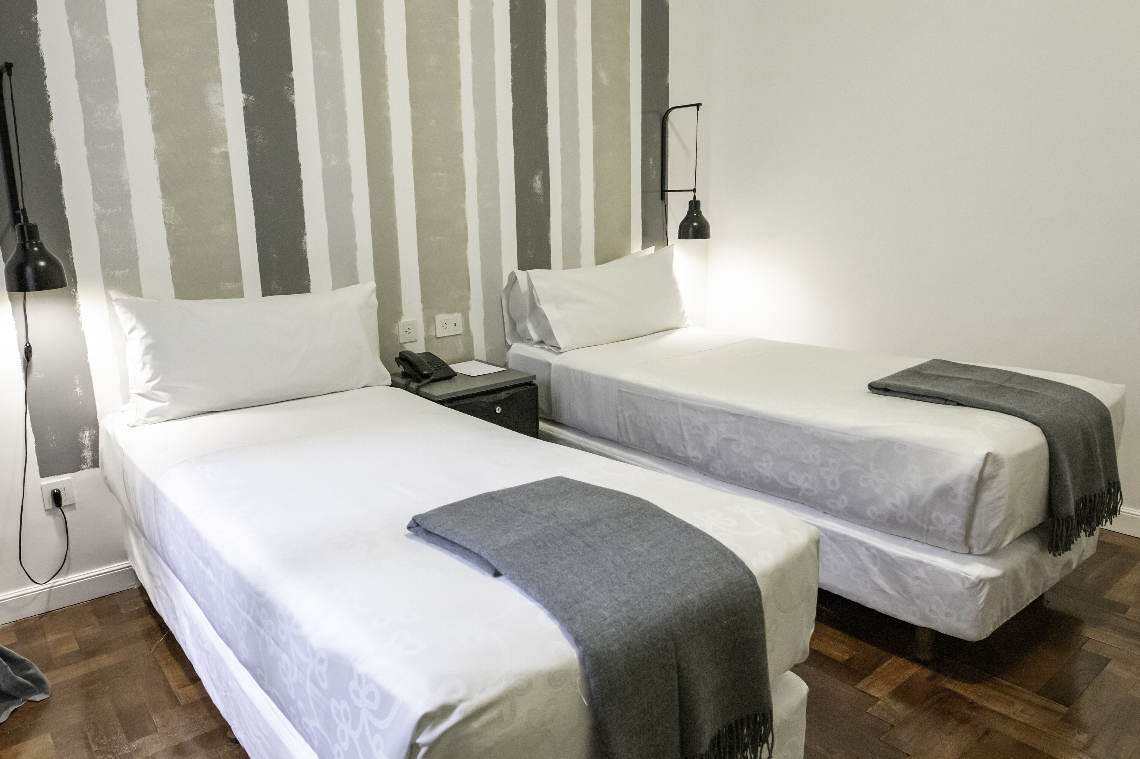 Une chambre avec deux lits, une table de chevet, une lampe et un mur à rayures verticales.