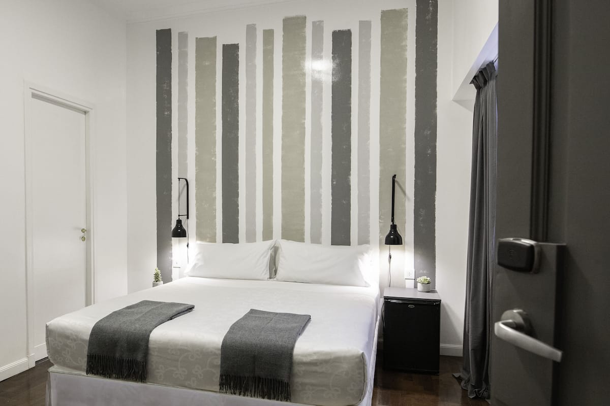 Een slaapkamer met een bed, nachtkastjes, een deur en een wand met verticale strepen.