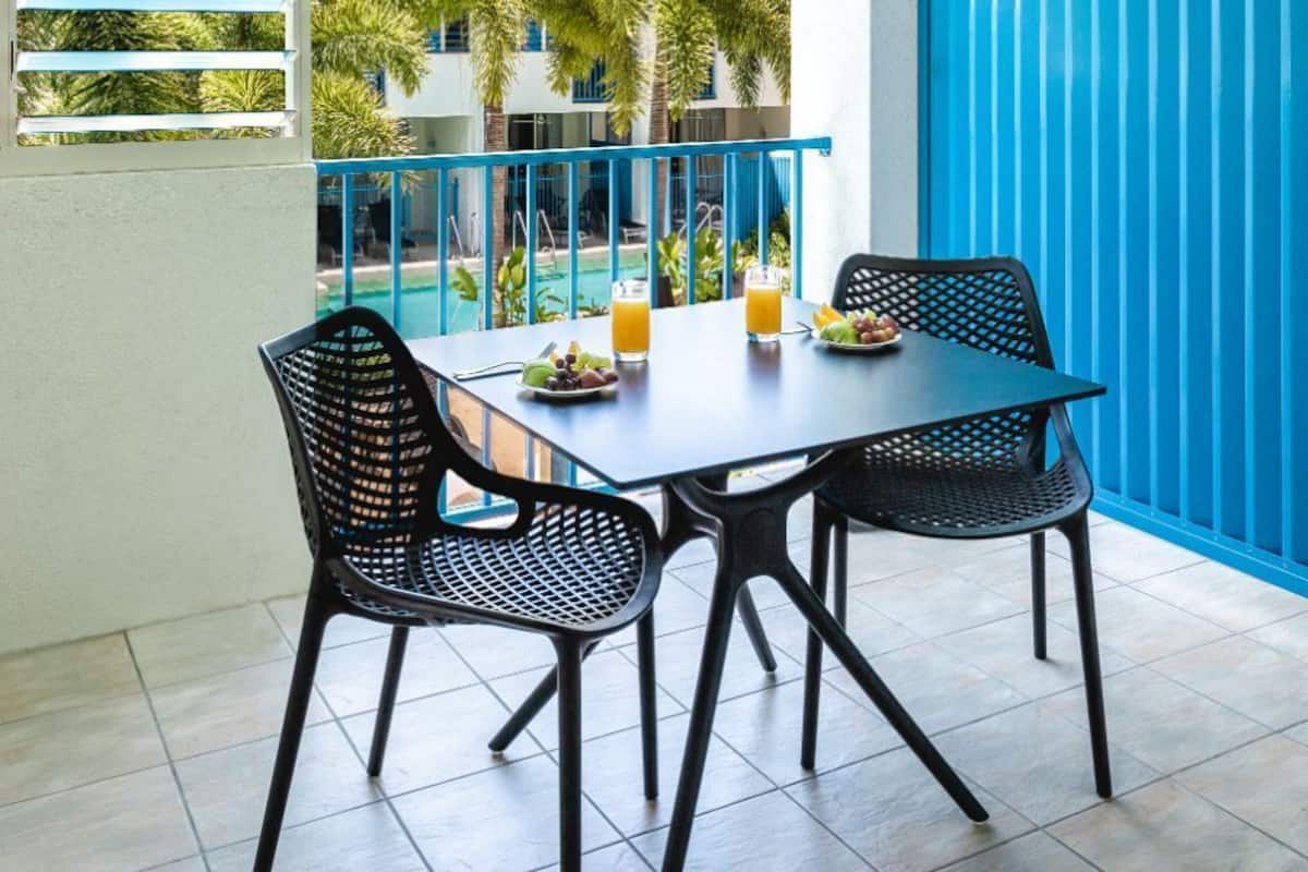 A balcony with a table and chairs, a blue fence, and a view of palm trees and buildings.