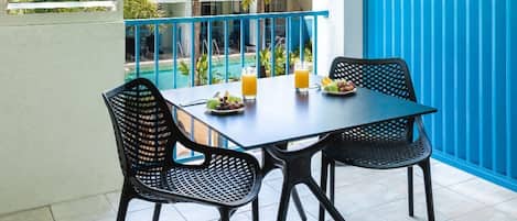 A balcony with a table and chairs, a blue fence, and a view of palm trees and buildings.