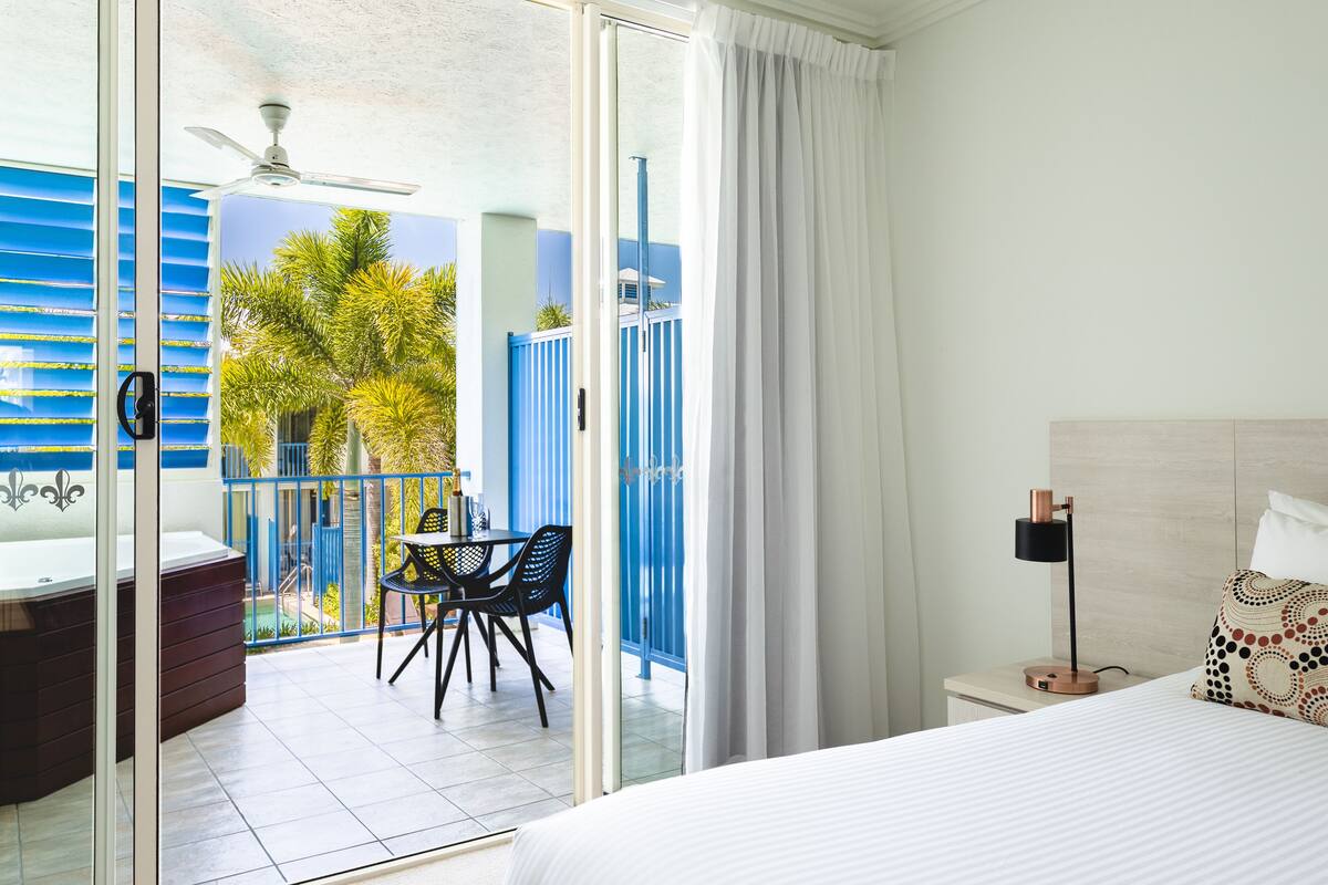A hotel room with a balcony, a bed, a nightstand, and a table with chairs.
