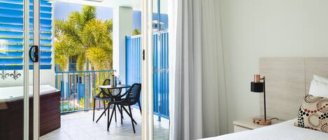 A hotel room with a balcony, a bed, a nightstand, and a table with chairs.