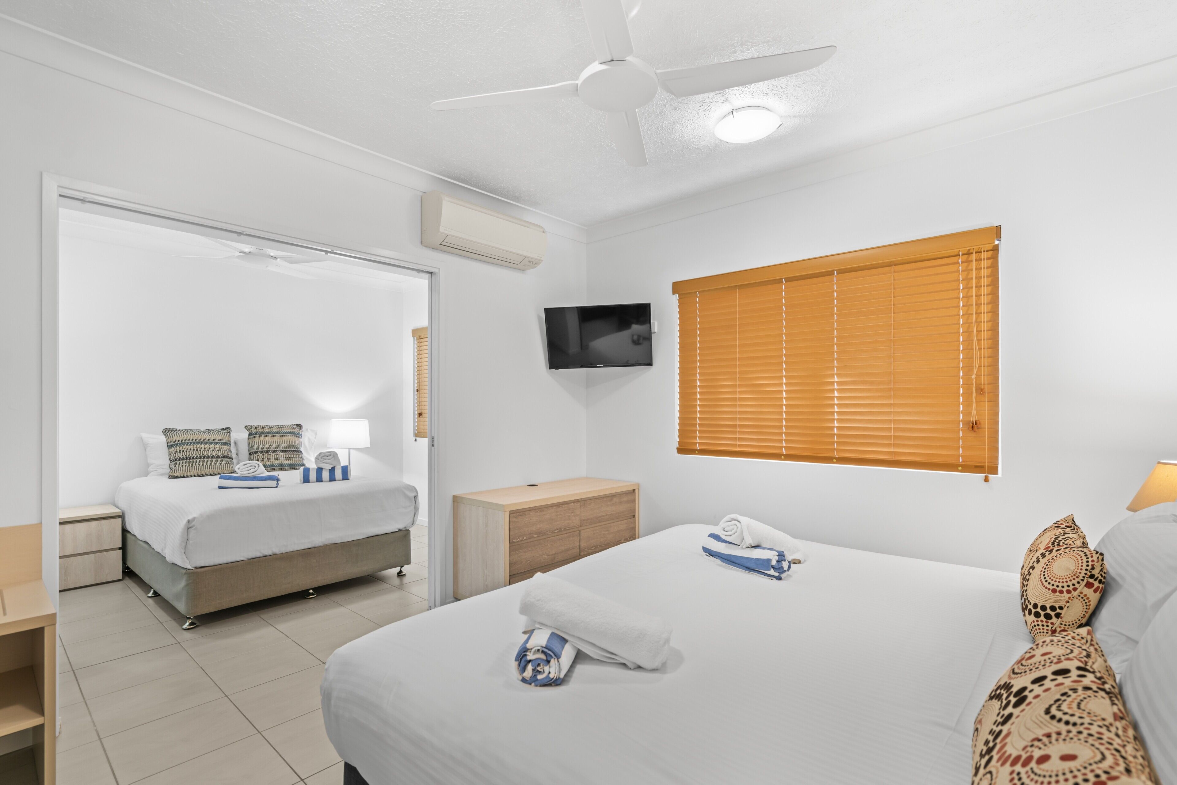A hotel room with a bed, a TV, a window with blinds, and a ceiling fan.