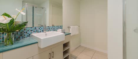A bathroom with a white sink, a glass shower enclosure, and a tiled backsplash.