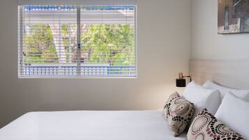 Una camera d'albergo con un'ampia finestra, un letto con lenzuola bianche e una lampada a parete.