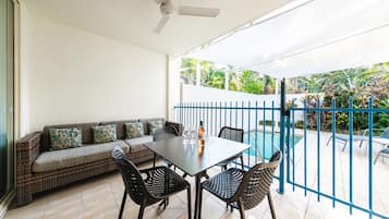 Un balcón con una mesa de comedor, sillas, un sofá con cojines y una piscina al fondo.