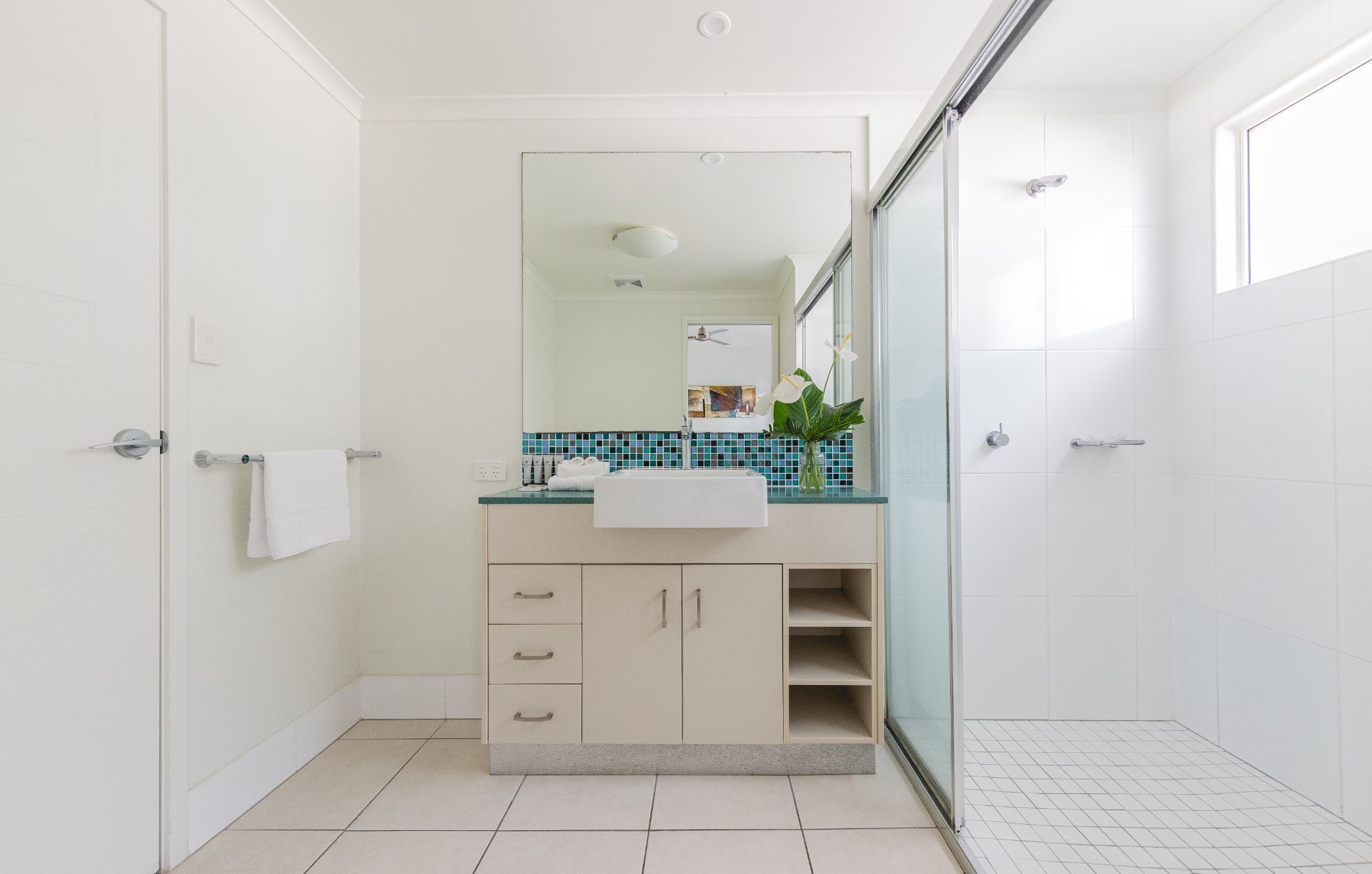 Un baño moderno con un lavabo blanco, un espejo y una cabina de ducha de vidrio.