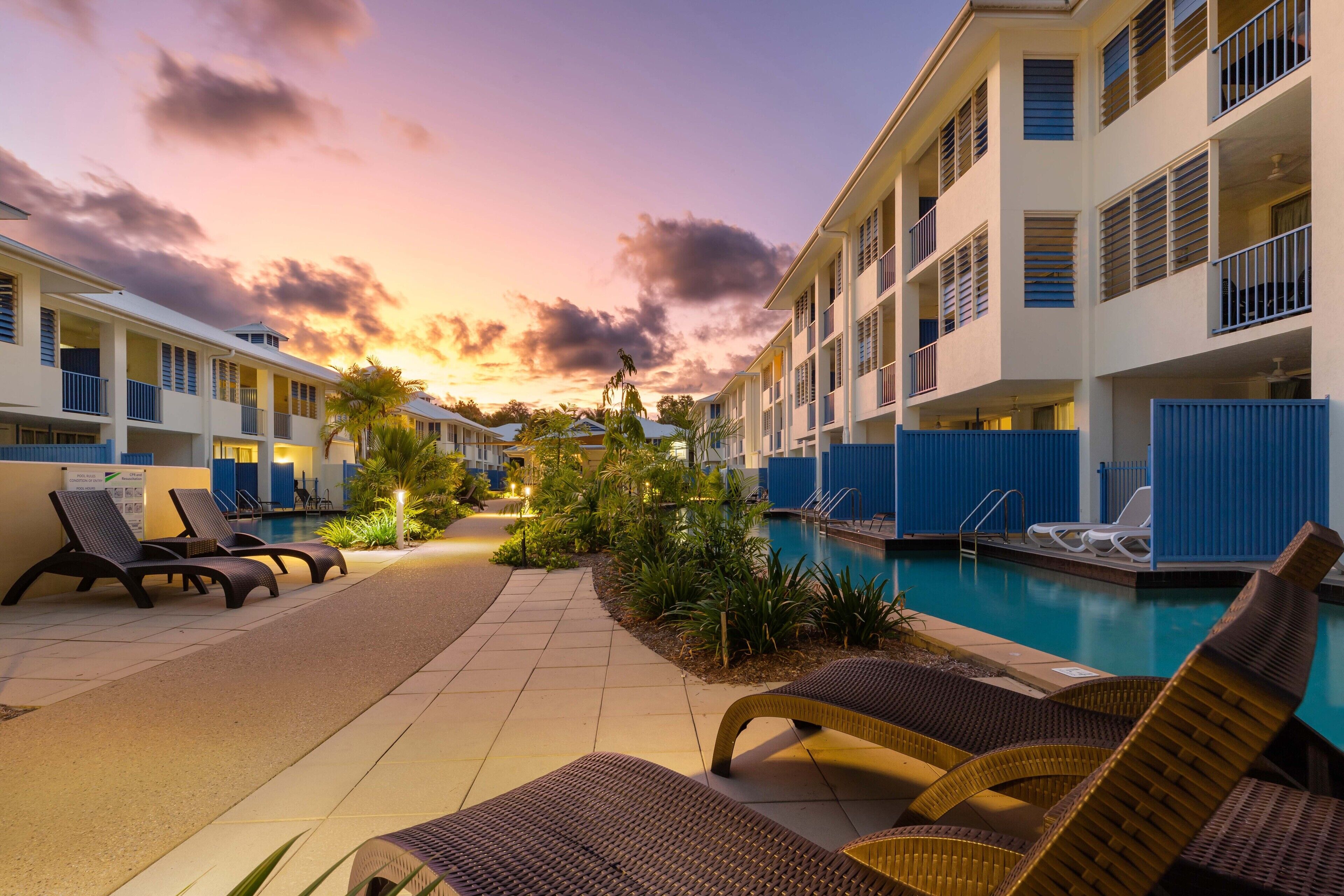 A hotel pool area with lounge chairs and a swimming pool, surrounded by buildings with balconies.