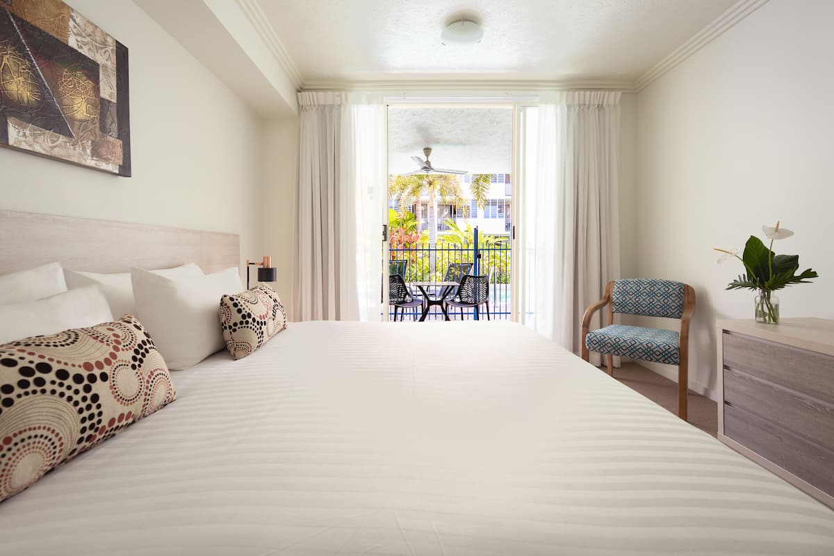 A hotel room with a large bed, a chair, a small table, and a view of the outside balcony.