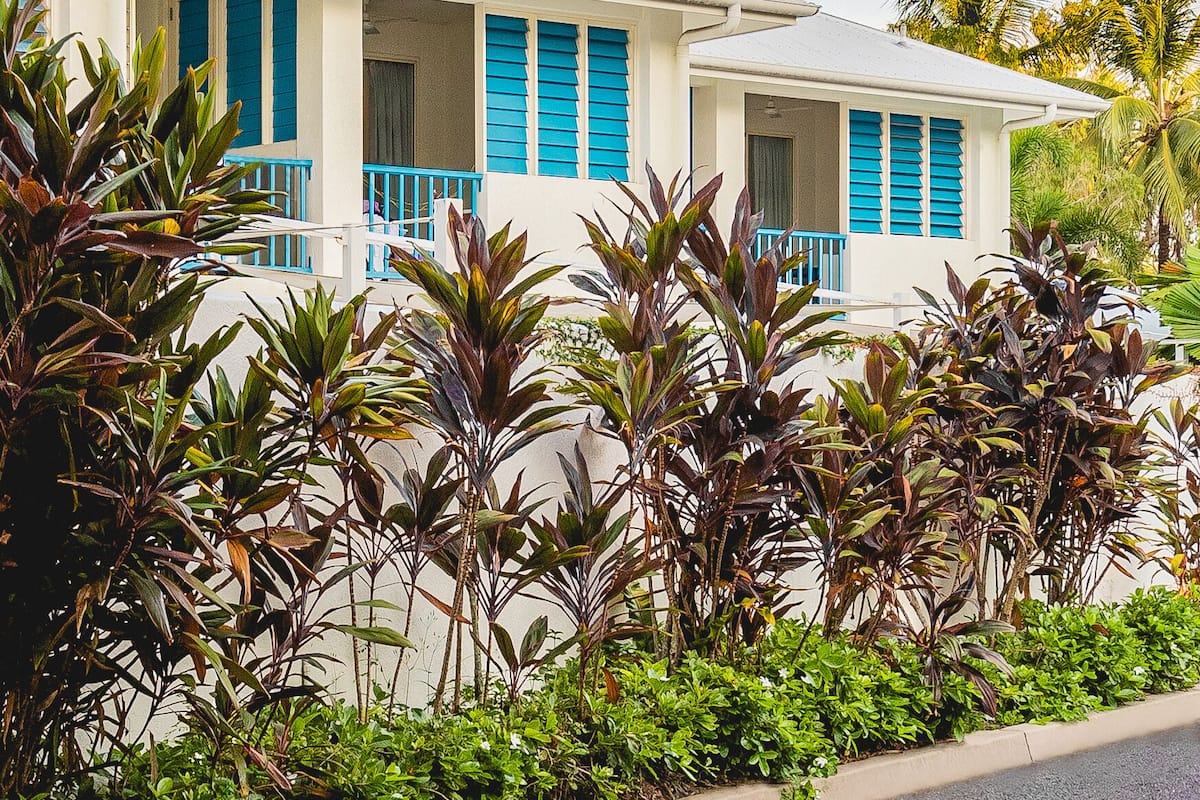A two-story house with a balcony, surrounded by tropical plants.