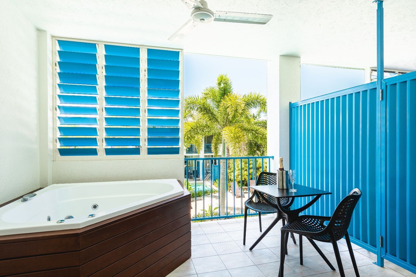 A room with a hot tub, a table with chairs, and a view of palm trees.