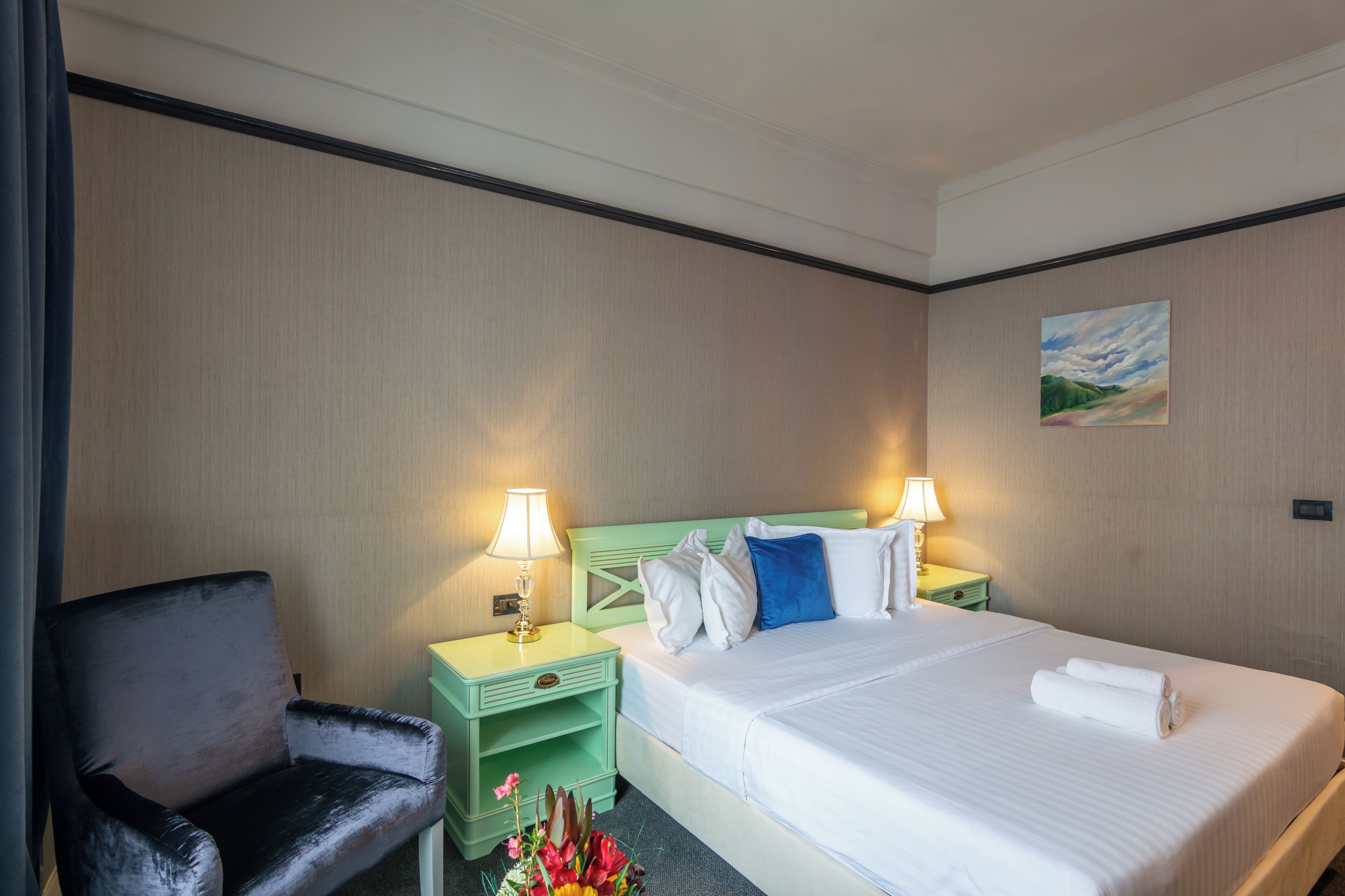 Et hotelværelse med seng, stol, natbord med lampe og et billede på væggen.