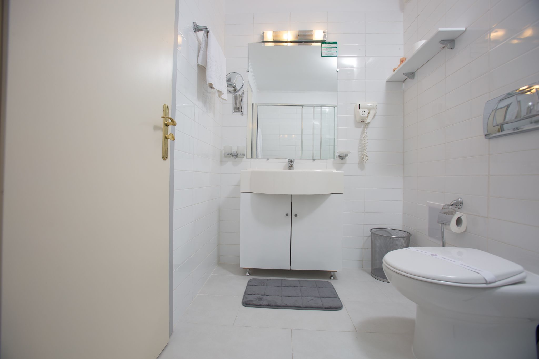 Un baño pequeño y limpio con lavamanos, espejo e inodoro blancos.