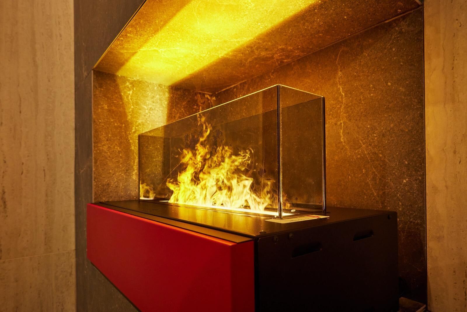 Una chimenea moderna con cerramiento de vidrio y base roja, frente a una pared con textura.