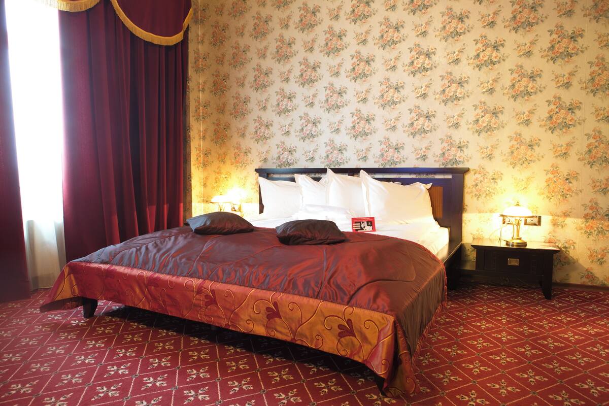 Uma cama bem arrumada com colcha vermelha, papel de parede estampado com flores e tapete vermelho.